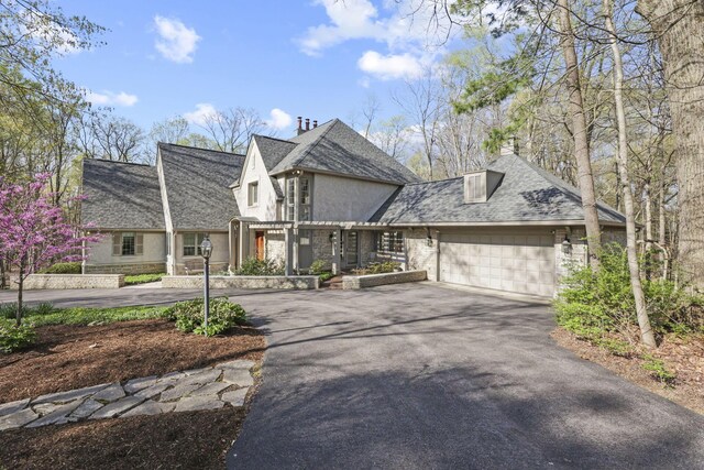 660 Woods Hollow Ln, Powell, OH 43065 - view of front facade featuring a chimney, stucco siding, aphalt driveway, a garage, and roof with shingles