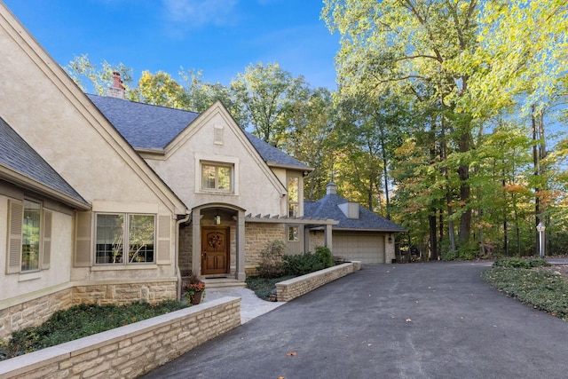 660 Woods Hollow Ln, Powell, OH 43065 - view of front of house with a garage, a chimney, stone siding, and aphalt driveway