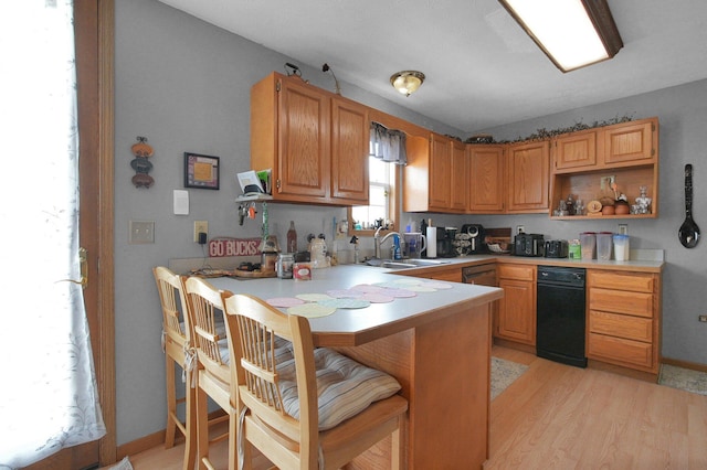kitchen featuring a sink, light wood finished floors, light countertops, a peninsula, and a kitchen bar