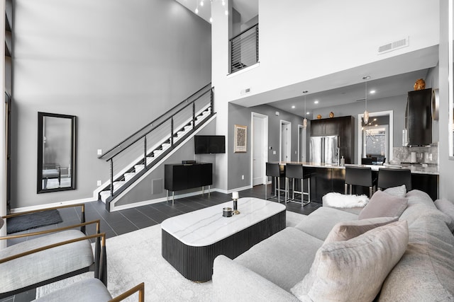 living area featuring visible vents, baseboards, a towering ceiling, and stairway