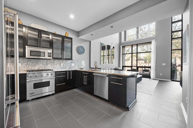 kitchen featuring appliances with stainless steel finishes, a sink, dark cabinetry, a peninsula, and tasteful backsplash