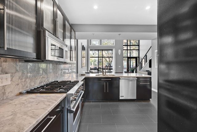 kitchen featuring appliances with stainless steel finishes, a sink, a peninsula, tasteful backsplash, and dark tile patterned flooring