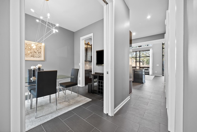 hall with baseboards, recessed lighting, dark tile patterned floors, and a chandelier