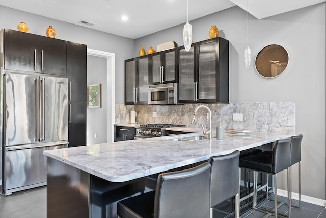 kitchen featuring decorative backsplash, a sink, light stone counters, a peninsula, and stainless steel appliances