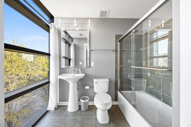 bathroom featuring toilet, tile patterned floors, baseboards, combined bath / shower with glass door, and visible vents