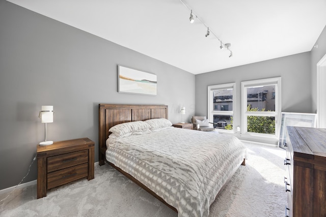 bedroom with light colored carpet, rail lighting, and baseboards