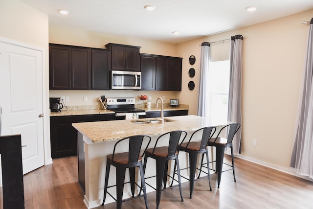 1151 Gelbray Dr, Columbus, OH 43207 - kitchen with a kitchen island with sink, a kitchen bar, appliances with stainless steel finishes, light stone countertops, and a sink