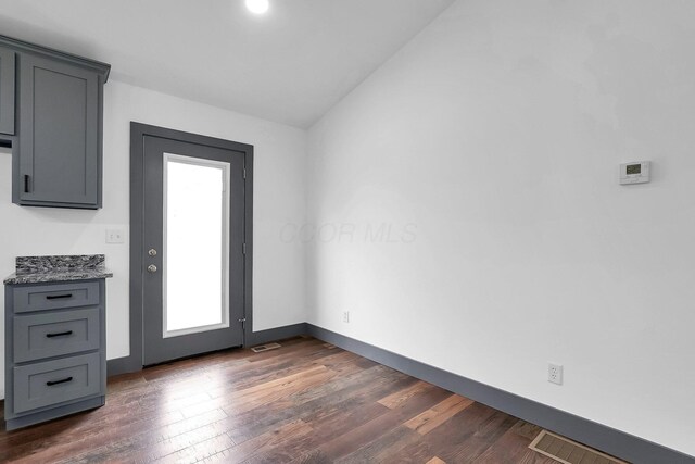 doorway with dark wood-style flooring, visible vents, vaulted ceiling, and baseboards