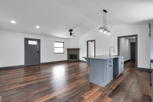kitchen featuring light stone countertops, a sink, a glass covered fireplace, a ceiling fan, and lofted ceiling