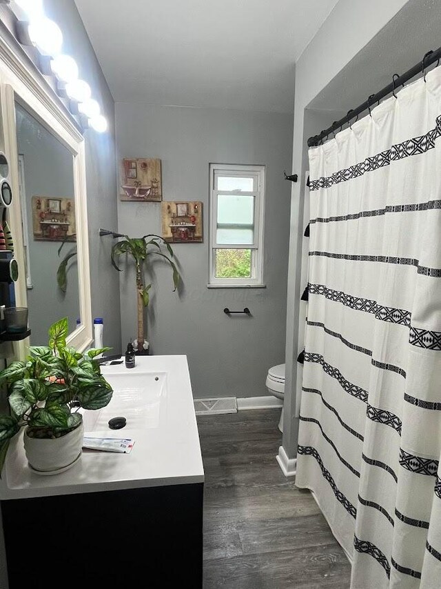 bathroom with a shower with shower curtain, baseboards, toilet, wood finished floors, and vanity