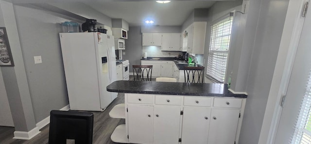 kitchen featuring dark wood-style flooring, white appliances, a peninsula, white cabinetry, and baseboards