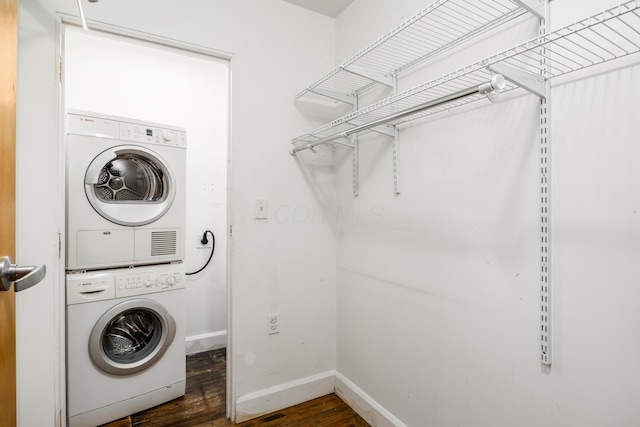 clothes washing area with baseboards, laundry area, stacked washer / dryer, and wood finished floors