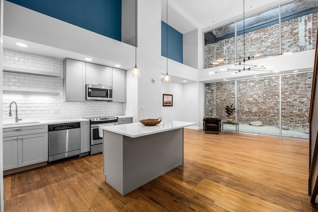 kitchen with gray cabinets, a towering ceiling, appliances with stainless steel finishes, a sink, and light countertops