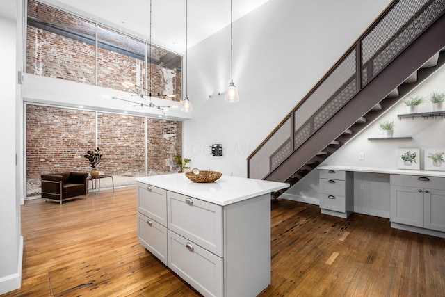 kitchen featuring brick wall, gray cabinetry, hardwood / wood-style flooring, and a towering ceiling