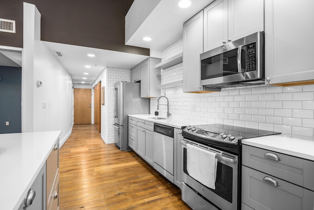 kitchen featuring a sink, gray cabinetry, open shelves, and stainless steel appliances