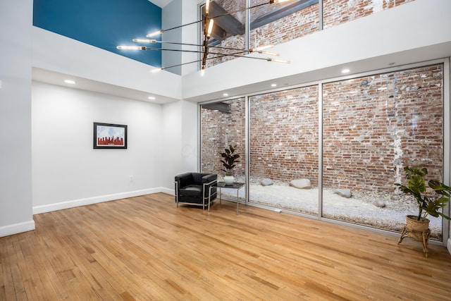 unfurnished room with a towering ceiling, brick wall, hardwood / wood-style floors, baseboards, and a chandelier