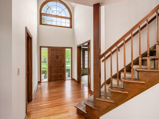 foyer entrance with baseboards, light wood finished floors, a towering ceiling, and stairway