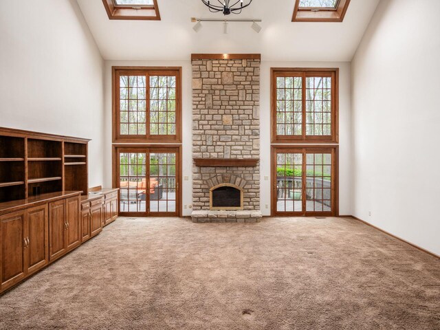 unfurnished living room featuring a skylight, light colored carpet, a healthy amount of sunlight, and high vaulted ceiling