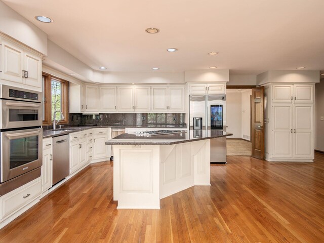 kitchen with decorative backsplash, a kitchen island, appliances with stainless steel finishes, a sink, and light wood-style floors