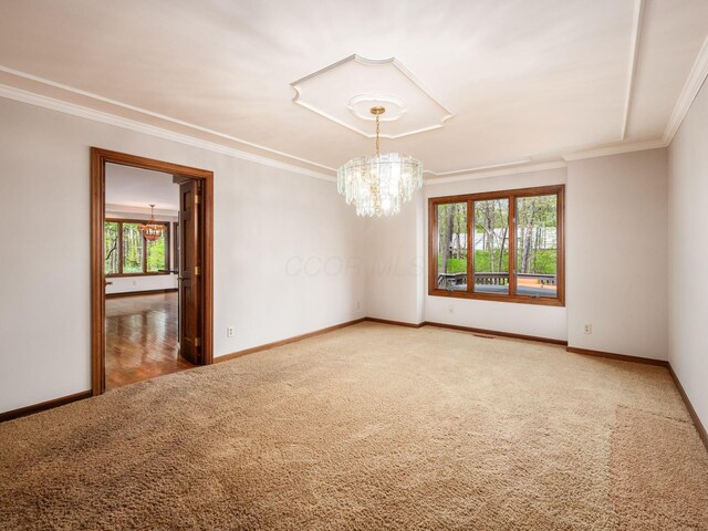 carpeted empty room with an inviting chandelier, ornamental molding, and baseboards