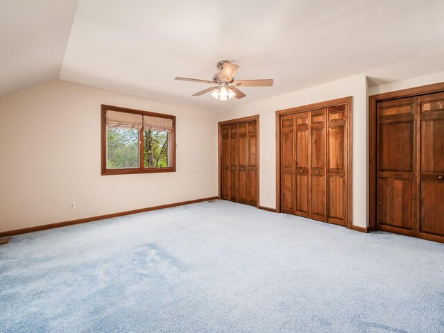 unfurnished bedroom with baseboards, a ceiling fan, multiple closets, and light carpet