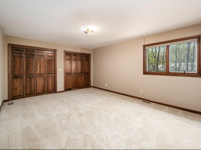 unfurnished bedroom featuring multiple closets, visible vents, light carpet, and baseboards