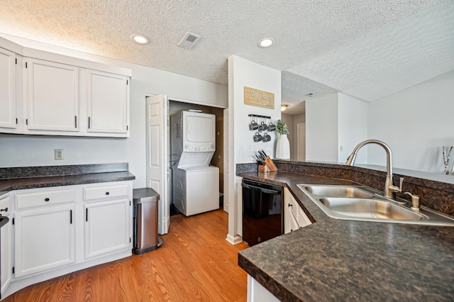 kitchen with stacked washer and dryer, a textured ceiling, a sink, dishwasher, and light wood finished floors