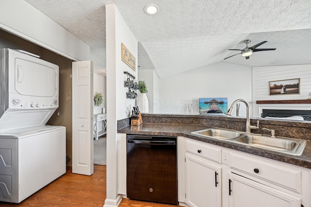 kitchen with a sink, stacked washer / drying machine, ceiling fan, light wood finished floors, and black dishwasher