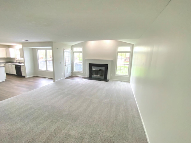 unfurnished living room with baseboards, a fireplace with flush hearth, light colored carpet, and a sink