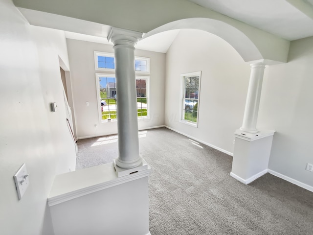 unfurnished living room featuring arched walkways, decorative columns, carpet floors, and baseboards