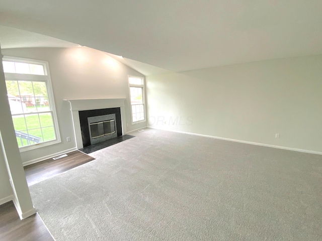 unfurnished living room featuring baseboards, a healthy amount of sunlight, a fireplace with flush hearth, and vaulted ceiling