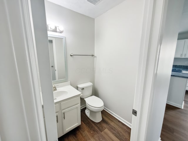 half bath with toilet, vanity, wood finished floors, and baseboards