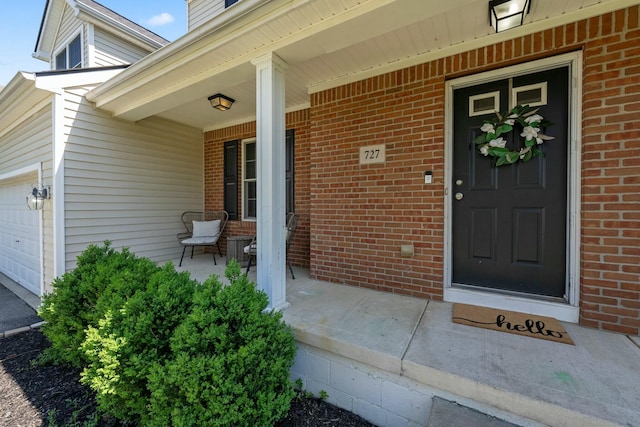 view of exterior entry featuring a porch, brick siding, and a garage