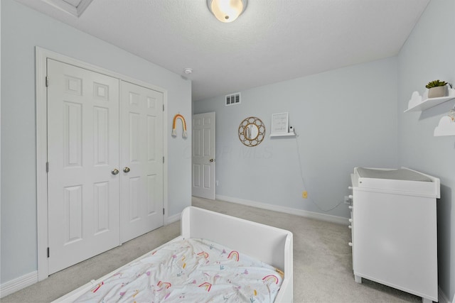 bedroom featuring visible vents, a closet, baseboards, light colored carpet, and a textured ceiling