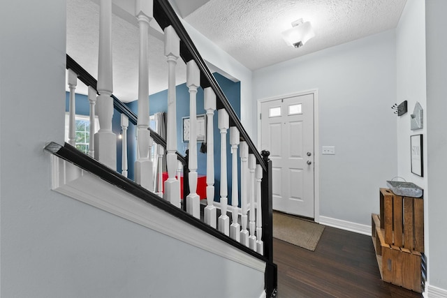 foyer featuring baseboards, a textured ceiling, wood finished floors, and stairway