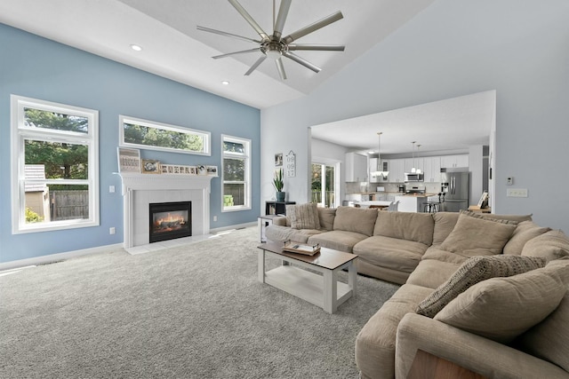 living area featuring a ceiling fan, a tiled fireplace, carpet floors, a high ceiling, and recessed lighting