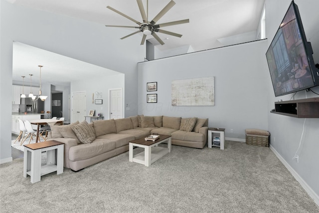 living room featuring baseboards, ceiling fan with notable chandelier, a high ceiling, and light carpet