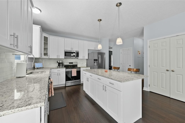 kitchen with dark wood-style floors, white cabinets, tasteful backsplash, a sink, and stainless steel appliances