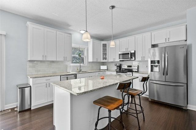 kitchen featuring white cabinets, dark wood-style flooring, appliances with stainless steel finishes, a center island, and tasteful backsplash