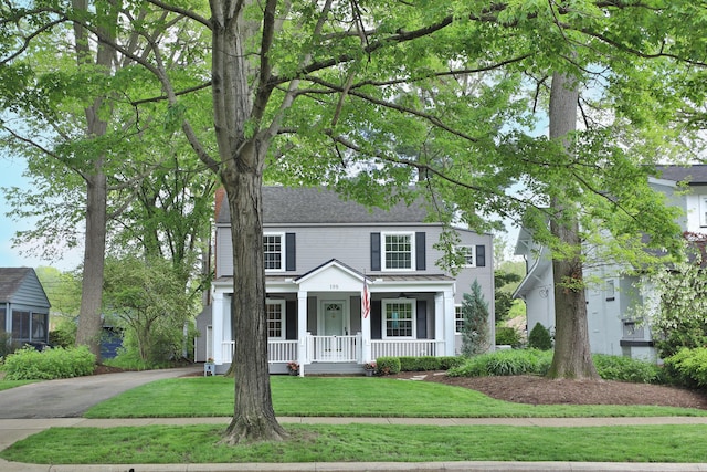 traditional-style house featuring a porch, a front lawn, and driveway