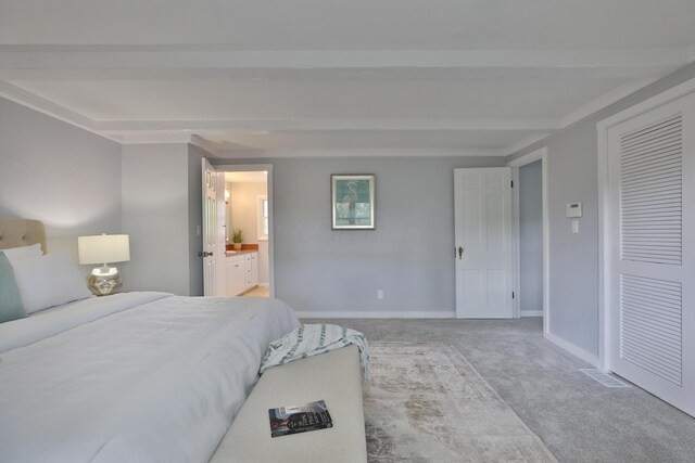 bedroom with carpet floors, baseboards, beamed ceiling, ensuite bathroom, and a closet