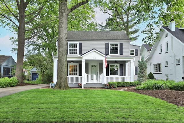 traditional home featuring covered porch, a front lawn, and a ceiling fan