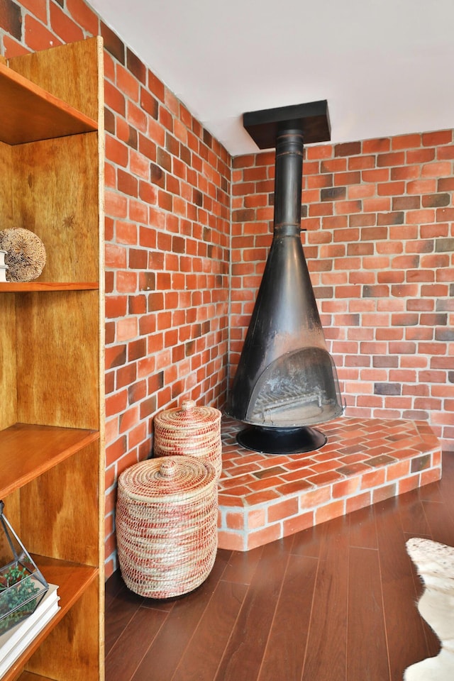 detailed view of a wood stove, wood finished floors, and brick wall
