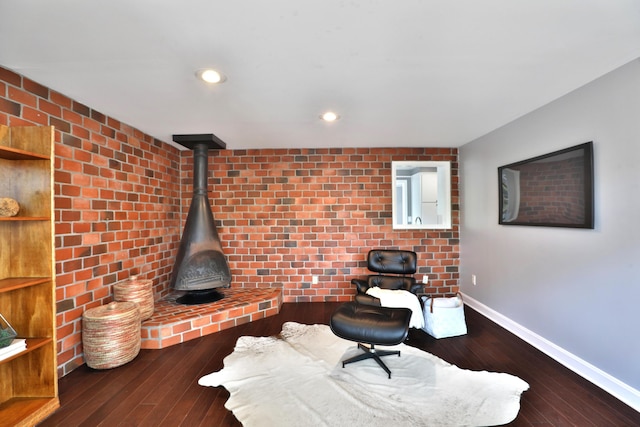 sitting room featuring baseboards, hardwood / wood-style flooring, brick wall, recessed lighting, and a wood stove
