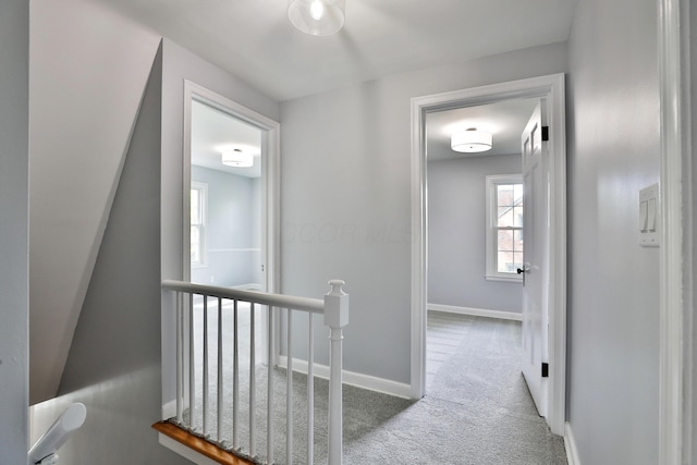 hallway featuring an upstairs landing, carpet floors, and baseboards