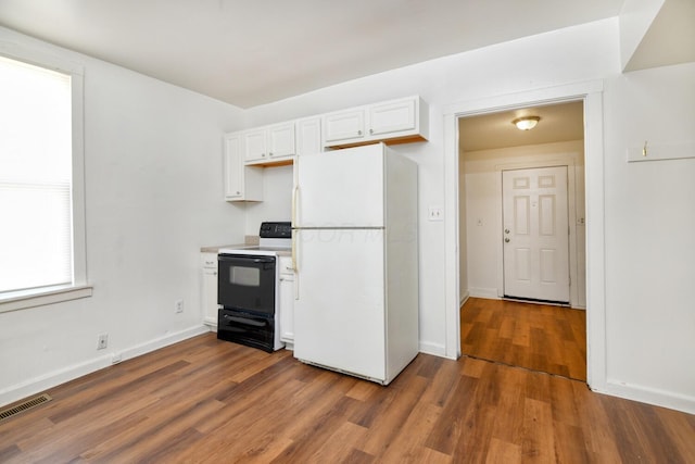 kitchen with dark wood finished floors, freestanding refrigerator, white cabinets, visible vents, and black range with electric cooktop