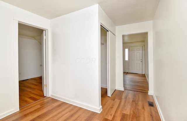 corridor featuring visible vents, light wood-style flooring, and baseboards