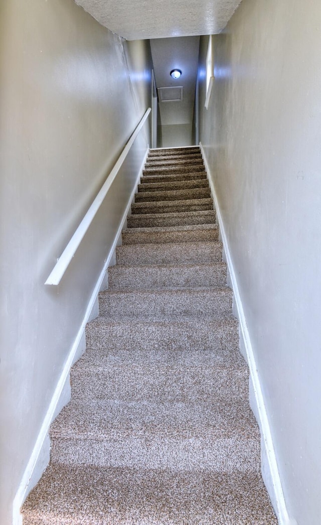 stairway featuring a textured ceiling, baseboards, and carpet floors