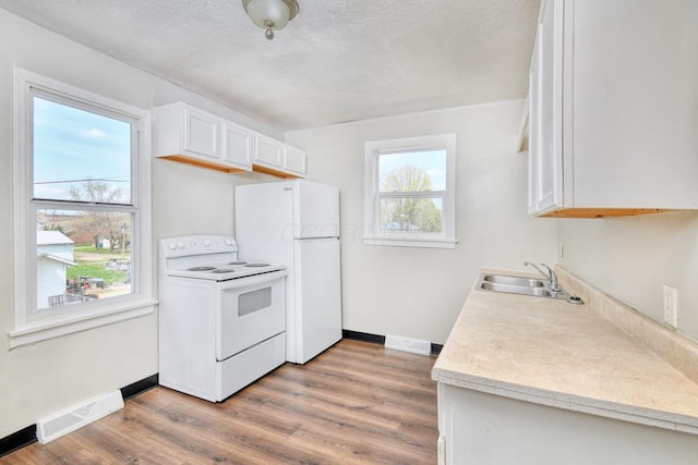 kitchen with wood finished floors, white appliances, a sink, baseboards, and visible vents