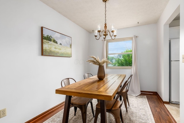 dining space featuring a chandelier, wood finished floors, baseboards, and a textured ceiling